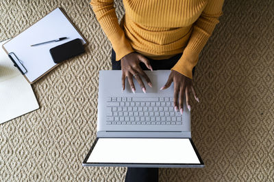 Young woman using laptop while sitting on carpet at at home