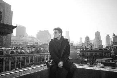 Portrait of young man sitting against buildings in city