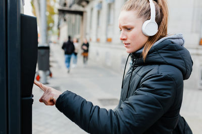 Young woman listening to music using parking meter