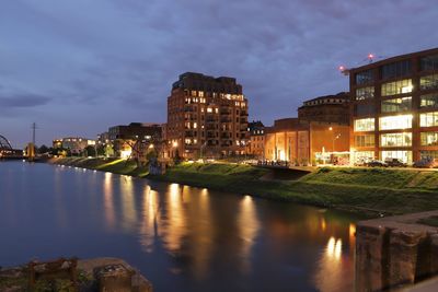 River by illuminated buildings against sky at dusk