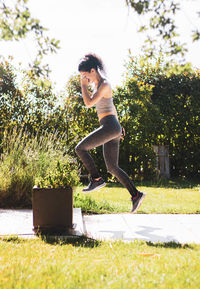 Side view of young woman jumping against trees