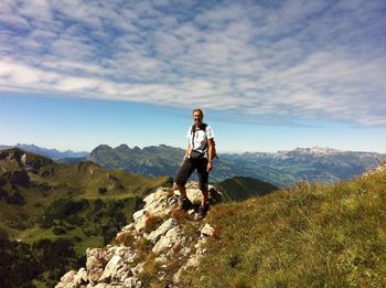 Happy female hiker standing on field at mountains against sky