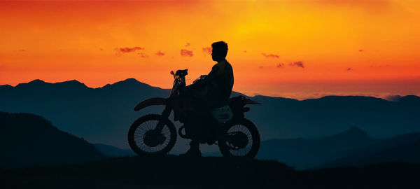 Man with motorcycle silhoutte with mountain background at sunset