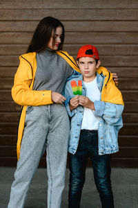 A girl in a yellow raincoat and a boy in a red cap are holding colorful ice cream in their hands