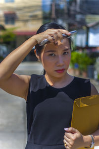 Portrait of a young woman holding camera while standing outdoors