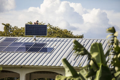 Construction worker carries solar panel on rooftop during install.