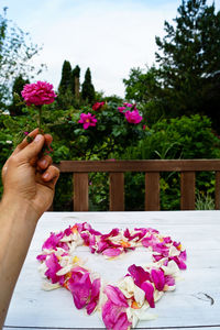 Cropped hand of man holding rose over heart shape petals at table