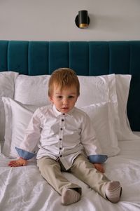 Little boy dressed for celebration sitting on a bed