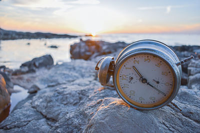 Close-up of clock on rock by sea against sky