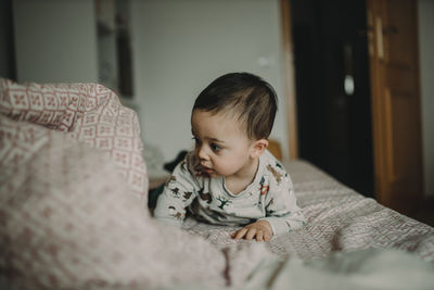 Cute boy looking away while relaxing on bed at home