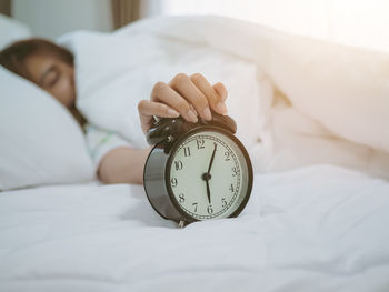 Woman snoozing alarm clock while sleeping on bed at home