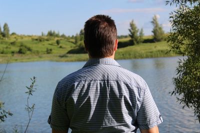Rear view of man looking at lake while standing against sky