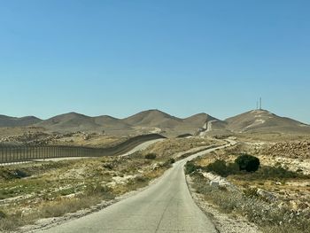 Road amidst desert against clear blue sky