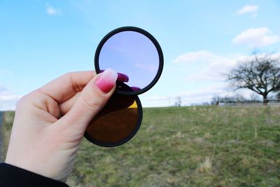 Close-up of hand holding eyeglasses against the sky