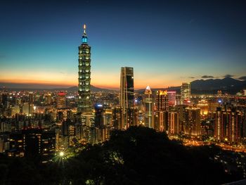 Taipei 101 against sky in illuminated city at dusk