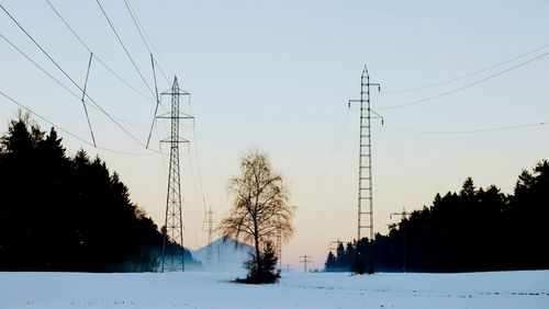 Electricity pylons on field against clear sky during winter