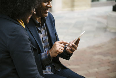 Happy woman looking at man using mobile phone in city