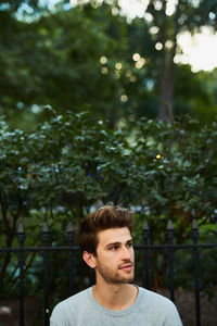 Young man looking away against trees