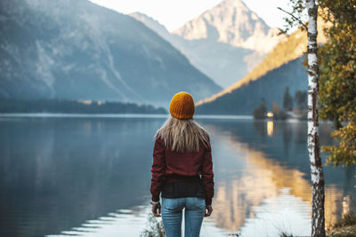 Rear view of woman standing by lake against mountain