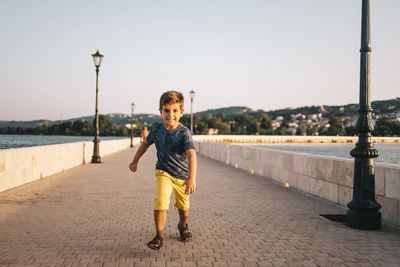 Portrait of smiling boy running on footpath against sky