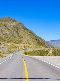 Road by mountain against clear blue sky
