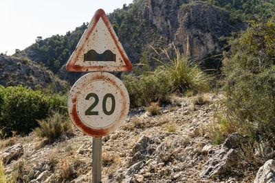 Old and worn traffic signs, with a natural mountainous background, on a sunny day.