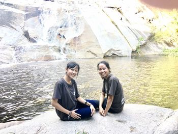 Portrait of young couple sitting on rock at shore