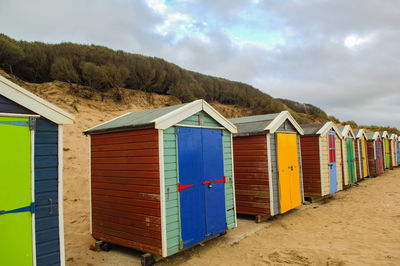 Beach huts by hill against sky