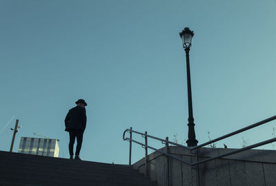 Silhouette of adult man in suit and hat standing on stairs against blue sky