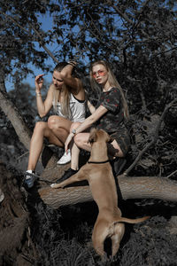 Female friends with dog sitting on log against trees in forest