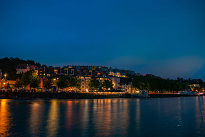 Illuminated buildings by river against sky at night