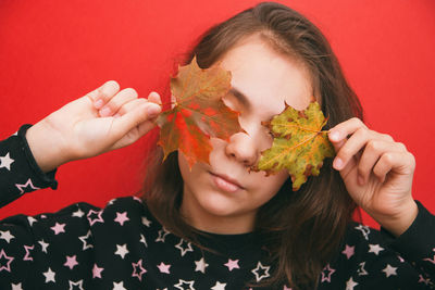 Girl holding autumn leaves against red wall