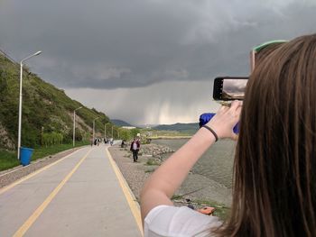 Rear view of woman photographing on road against sky
