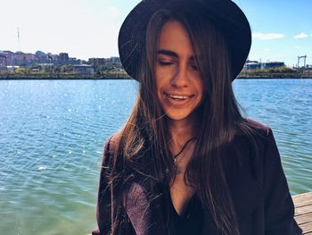 Smiling young woman standing against lake and sky