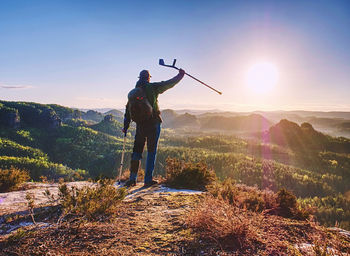 Hiker with medicine crutch achieved mountain peak. broken leg fixed in immobilizer, raised arm