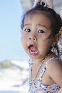 Close up of happy baby girl joy with opened mouth outdoor summer background. 