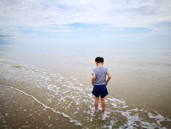 Rear view of boy standing on beach against sky