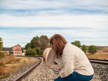 Side view of woman with luggage sitting on railroad track