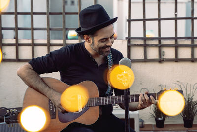 Portrait of young man wearing hat singing by microphone standing against sky