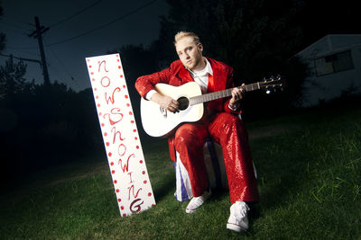 Portrait of man playing guitar while sitting on grassy field at night