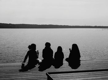 People sitting on pier over lake against sky