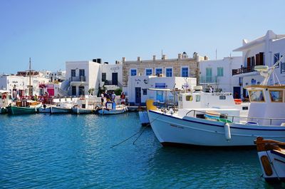 Sailboats moored on sea by buildings against clear sky