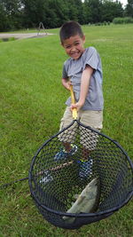 Full length of boy holding fishing net with fish while standing on grassy field