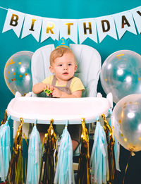 Cute baby boy sitting on high chair in birthday party