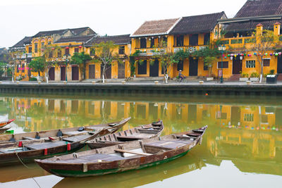 Boats moored in lake by houses against sky