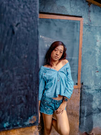 Portrait of young woman standing against wall