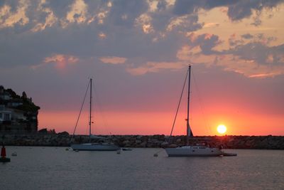 Sailboats sailing in sea against sky during sunset