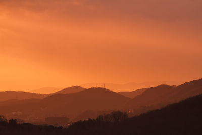 Scenic view of dramatic sky over silhouette mountains during sunset