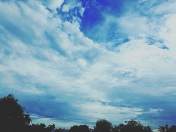 Low angle view of trees against cloudy sky