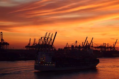 Ship in sea by commercial dock against sky during sunset